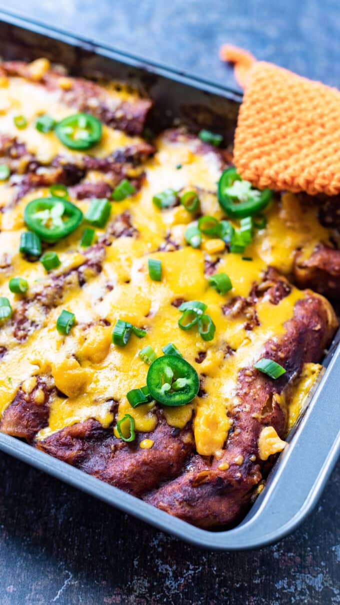 Portion of whole pan of enchiladas topped with jalapenos.