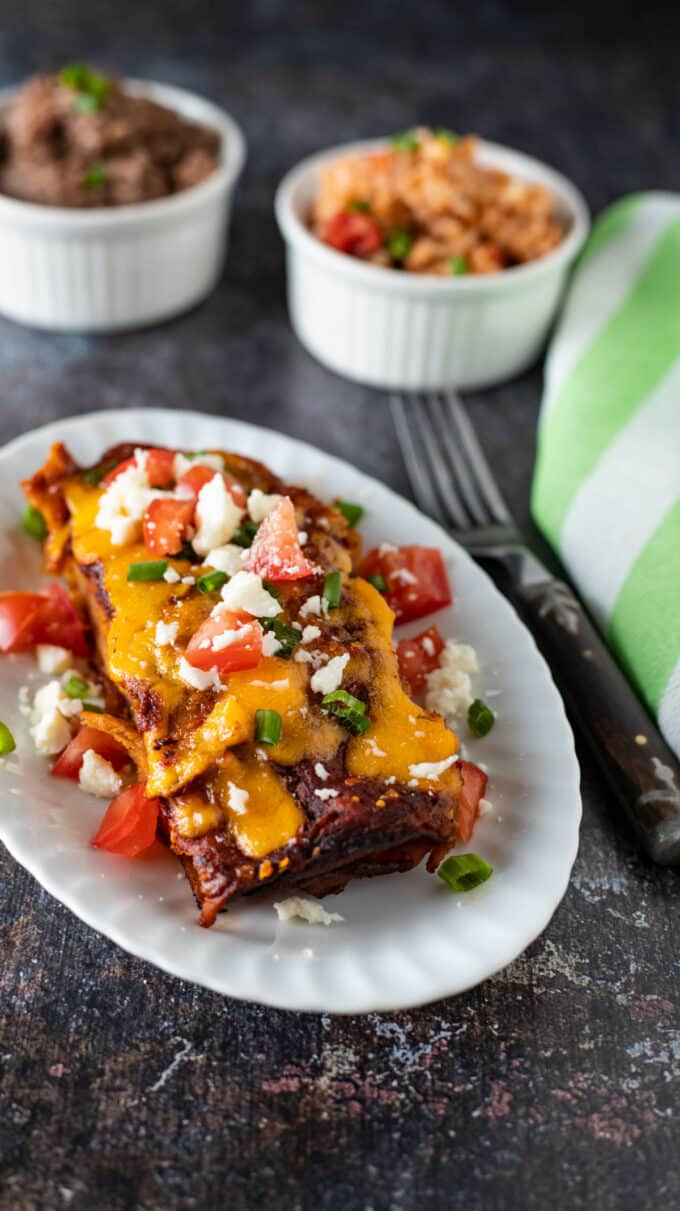 Two enchiladas on white plate with side dishes.