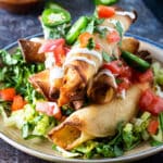 Stack of taquitos topped with colorful toppings.