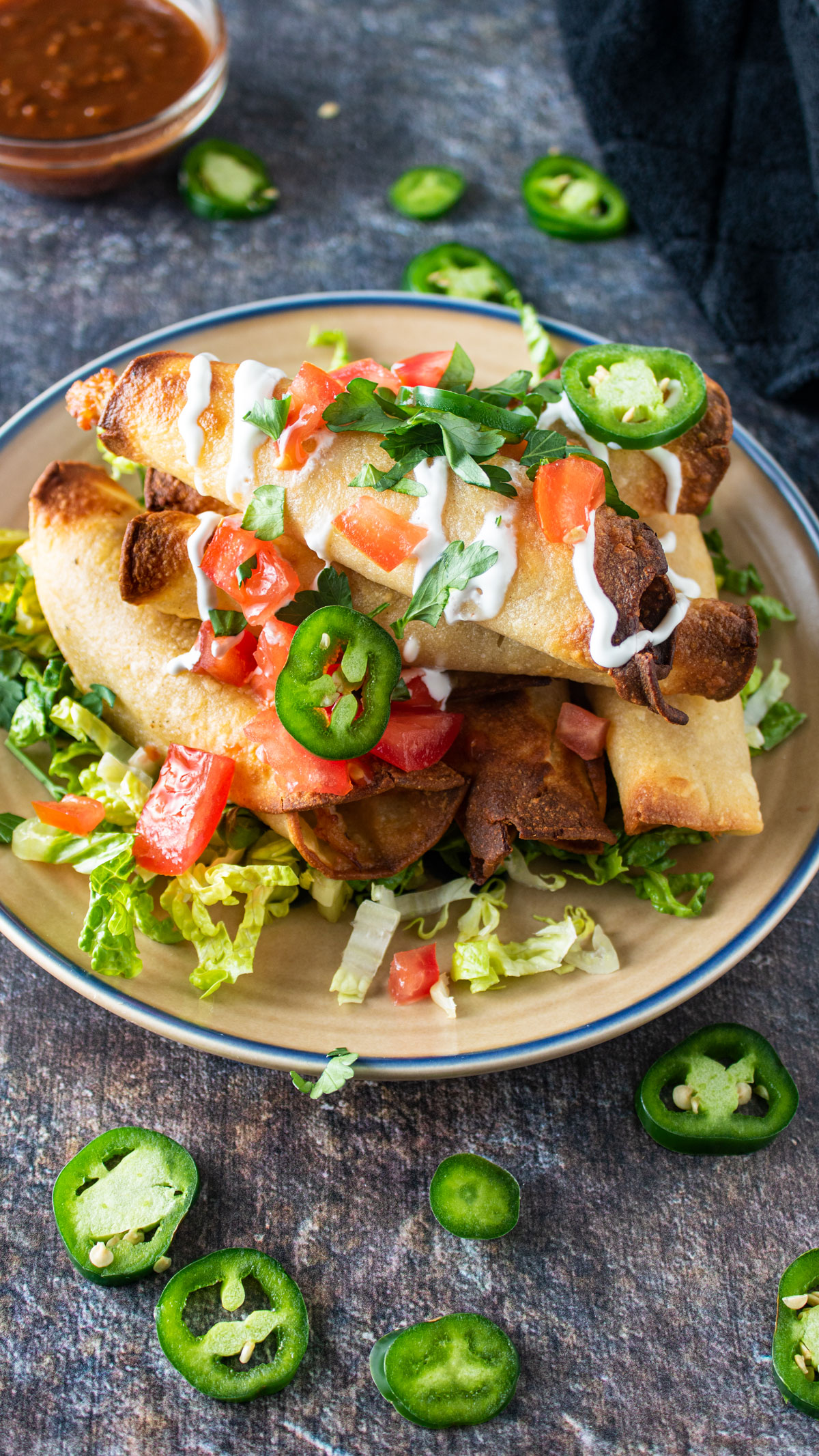 Pile of taquitos garnished with creme and vegetable.