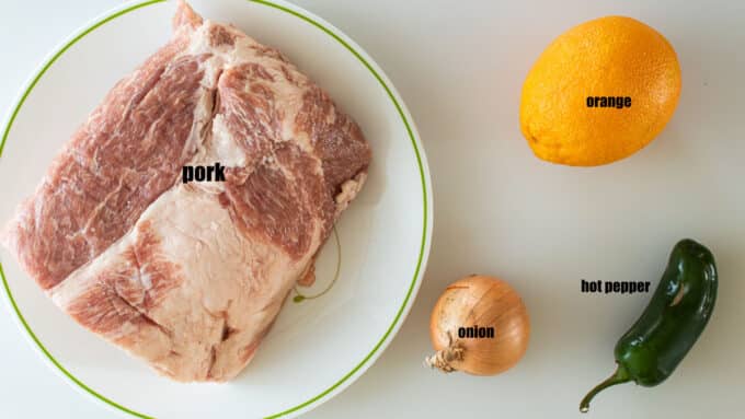 Ingredients for carnitas; pork, onion, orange, chile pepper.
