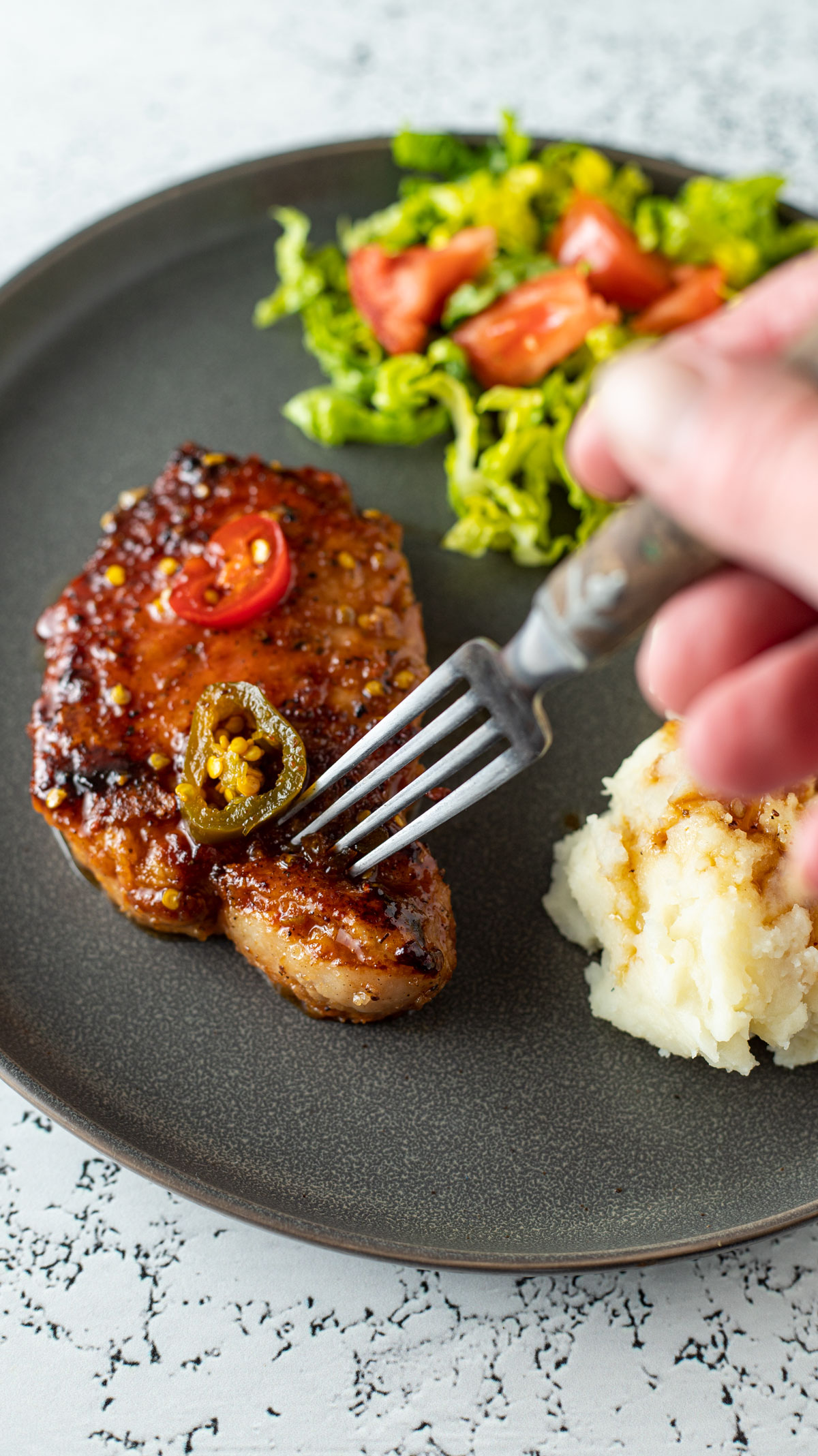 Pork chops coated with sweet and spicy jalapeno sauce Hand with fork piercing meat.