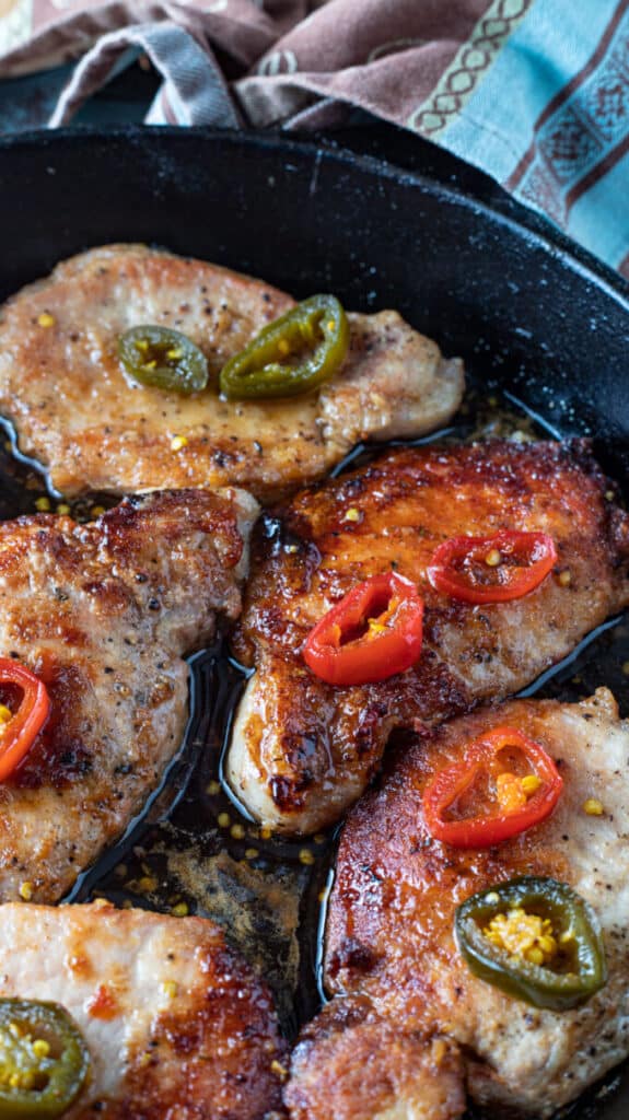 Glistening, golden Pork chops smothered in sweet and spicy jalapeno sauce Large cast iron pan with pork chops.