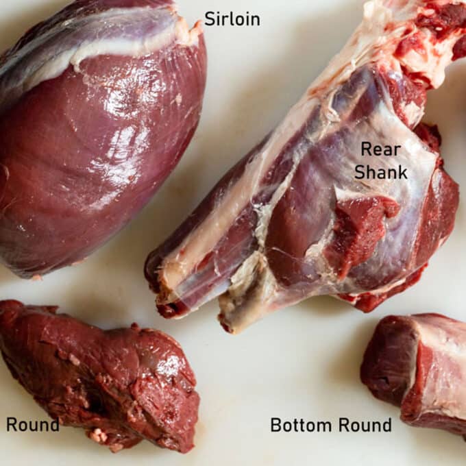 Individual raw cuts of venison on white board.