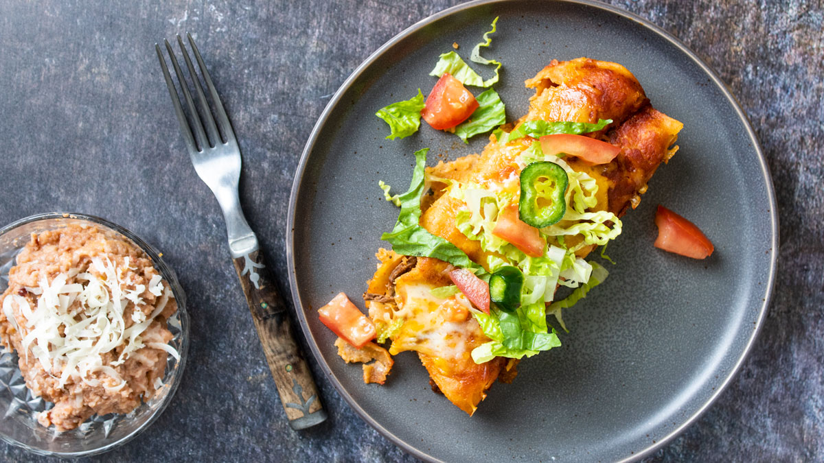 Two enchiladas on plate with lettuce tomato and pepper garnish
