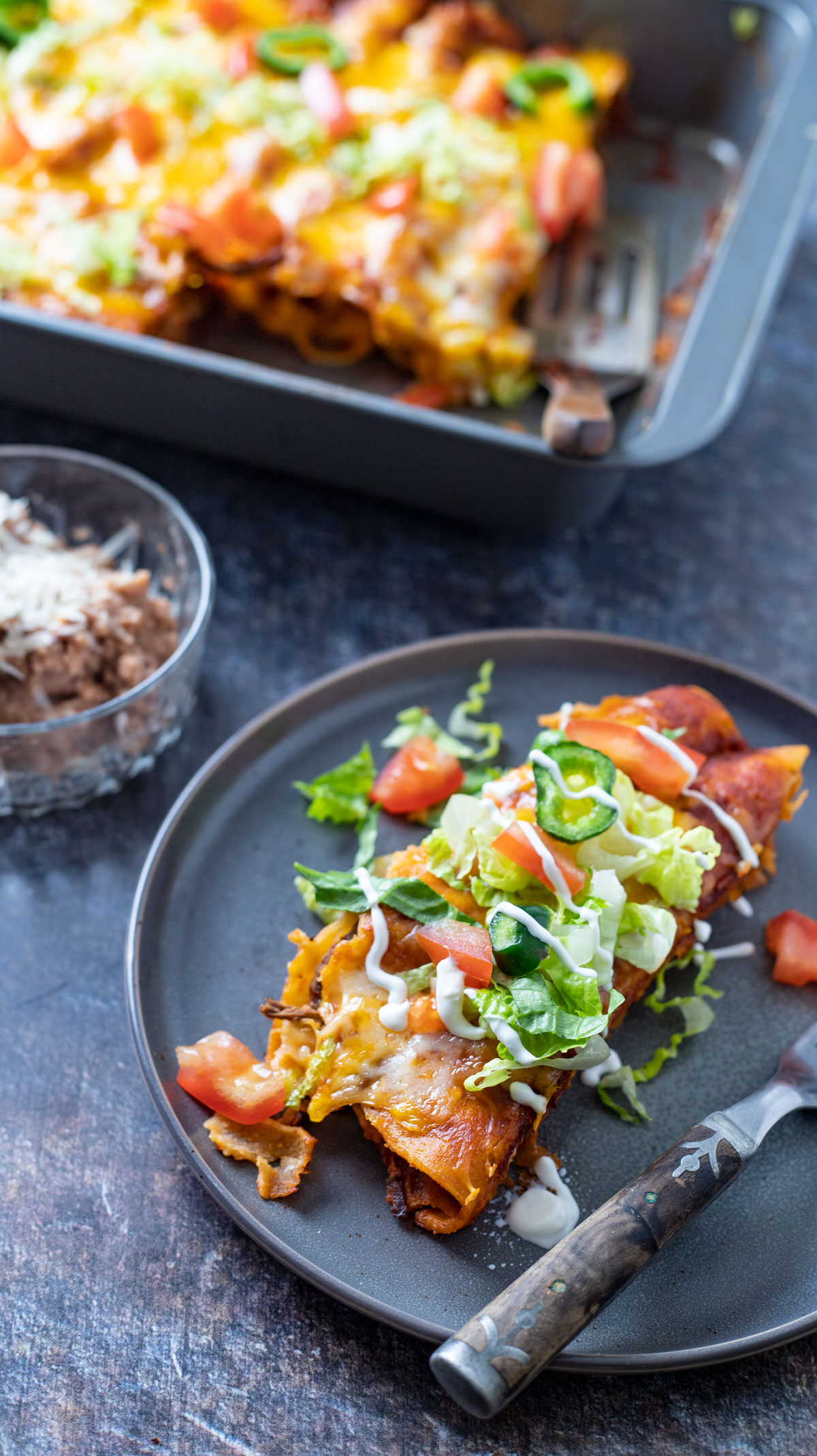 Enchiladas on gray plate drizzled with sour cream.