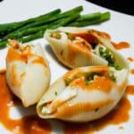 Pasta shells stuffed with seafood with vodka sauce topping and asparagus.