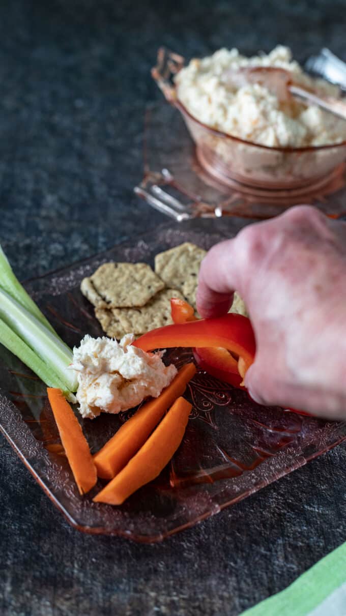 Plate of vegetables with hand scooping dip off of plate.