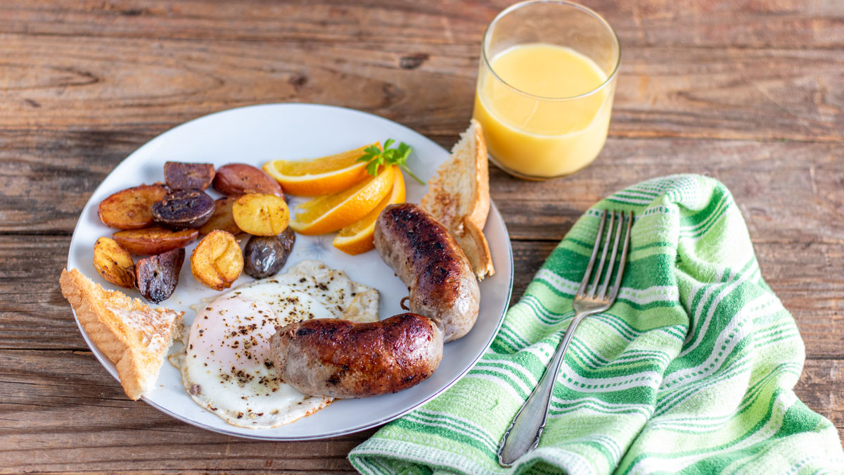 Eggs potatoes and sausage with toast and garnished with orange slices.