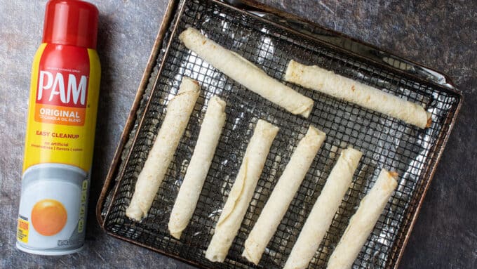 Taquitos on ait fryer basket with cooking spray on the side.