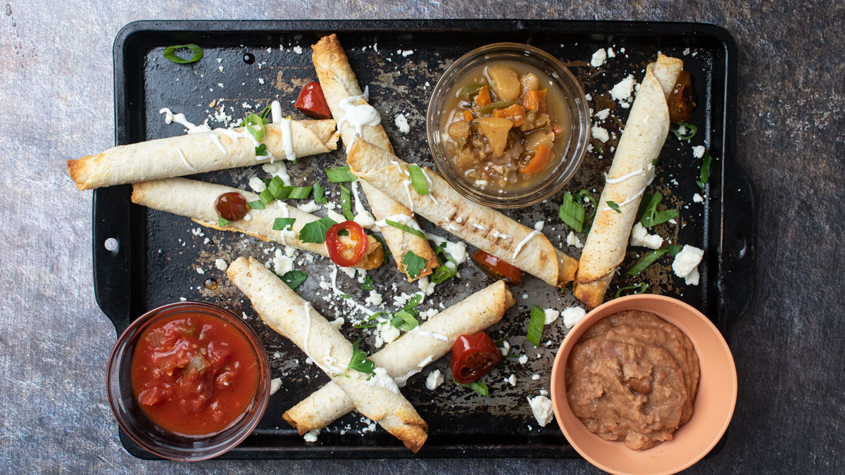 Overhead photo of taquitos with colorful toppings.