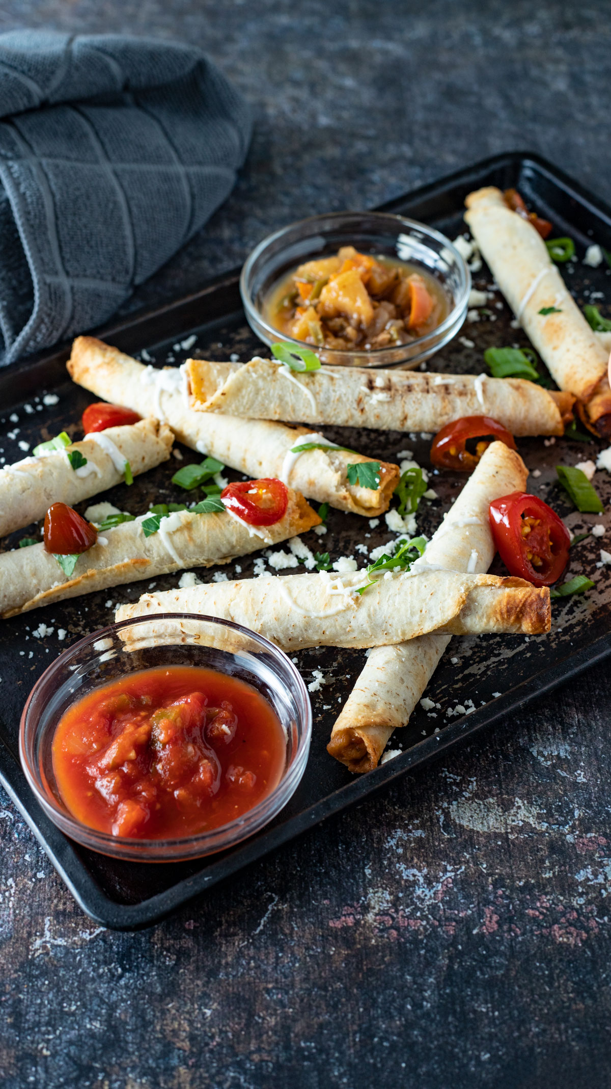 Metal tray stacked with taquitos and various toppings.
