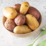 Boiled potatoes garnished with parsley in a beige bowl.