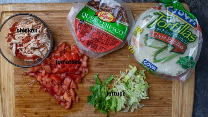 Ingredients for tacos; tortillas, cheese, chicken, lettuce and tomato.