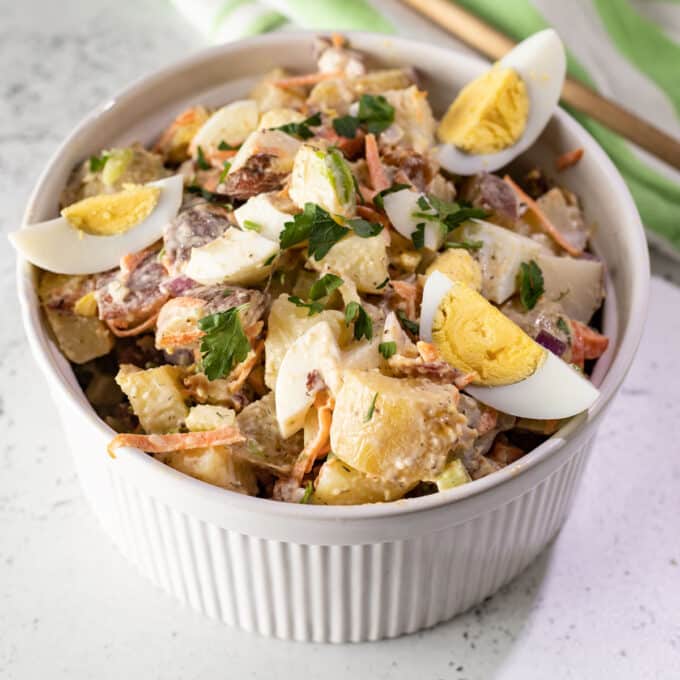 White bowl with potato salad with egg wedges and parsley garnish.