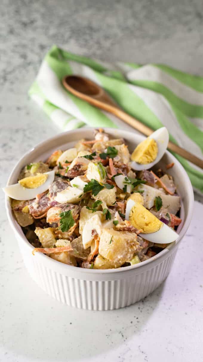 Potato salad in white bowl with green and white striped kitchen towel.