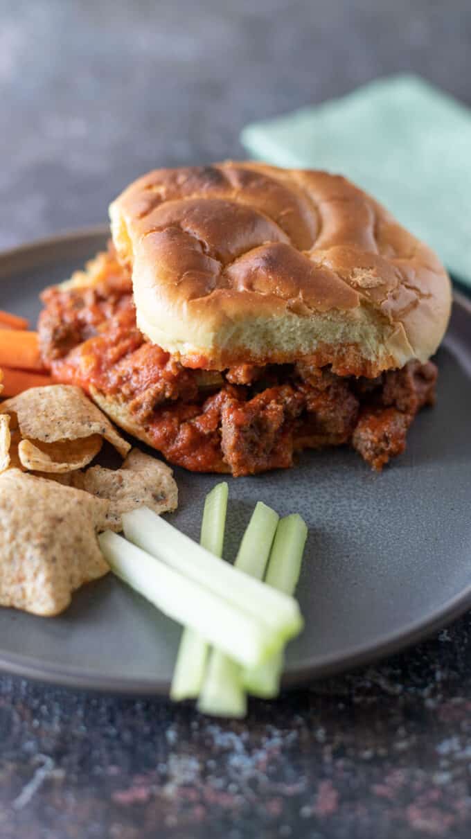 Sloppy joe on gray plate with chips and vegetables.