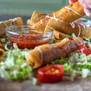 Woman's hand dunking taquitos in salsa.