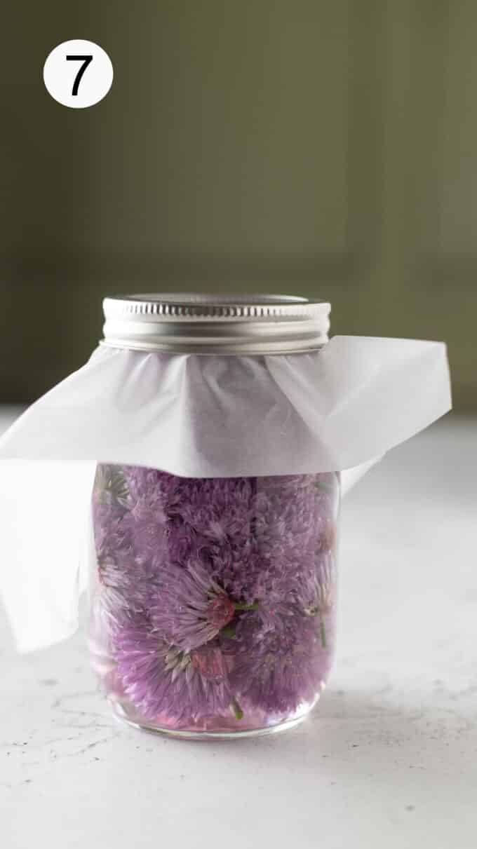 Jar of vinegar with fresh flowers with parchment paper and metal band securing the top.