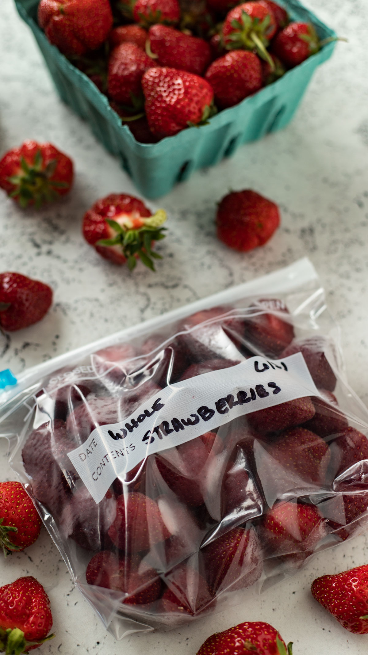Whole frozen strawberries in freezer bag with fresh berries on board.
