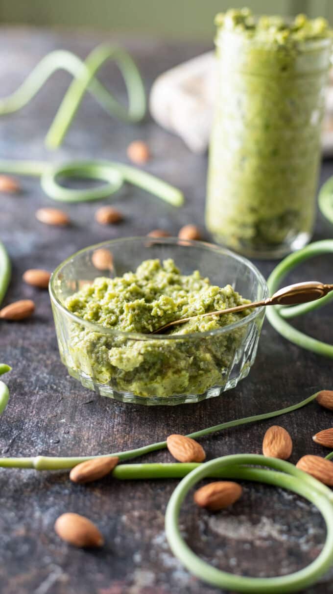 Jar and bowl of pesto with almonds and scapes garnish.
