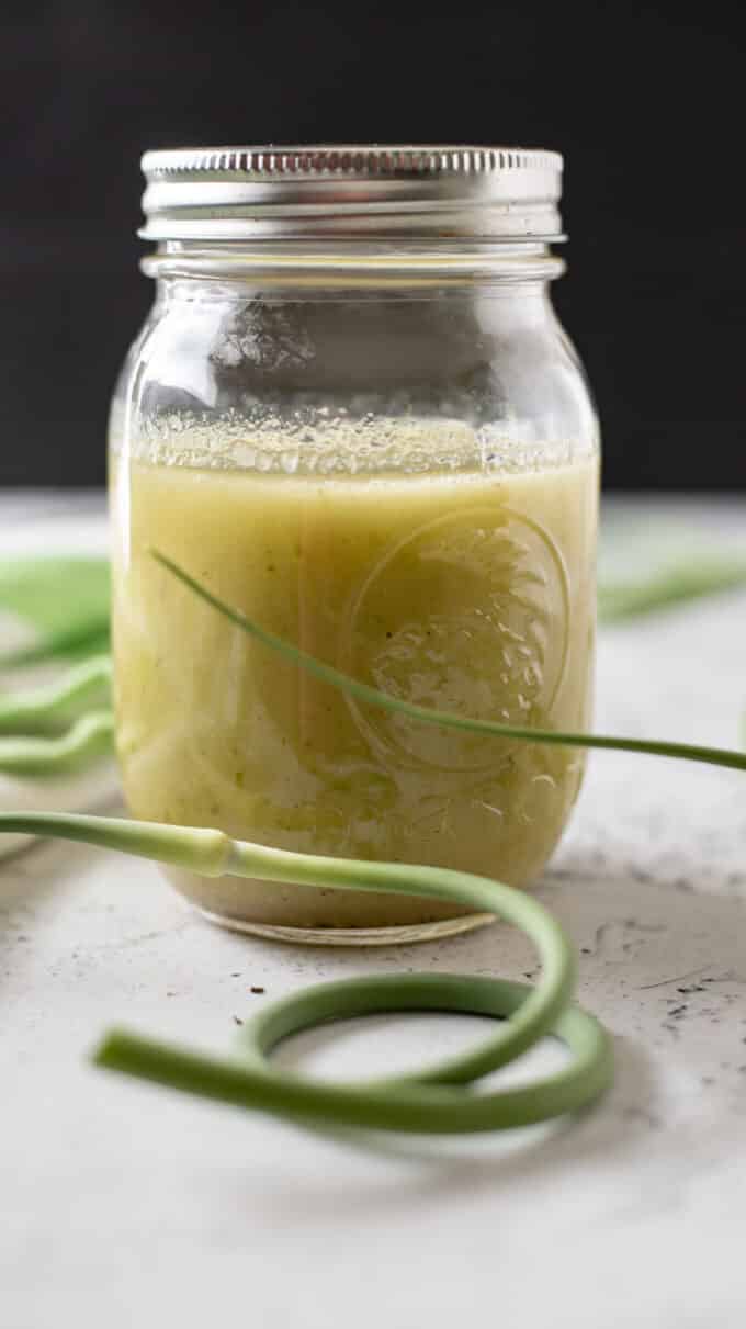 Vinaigrette in a pint canning jar with fresh garlic scapes around it.