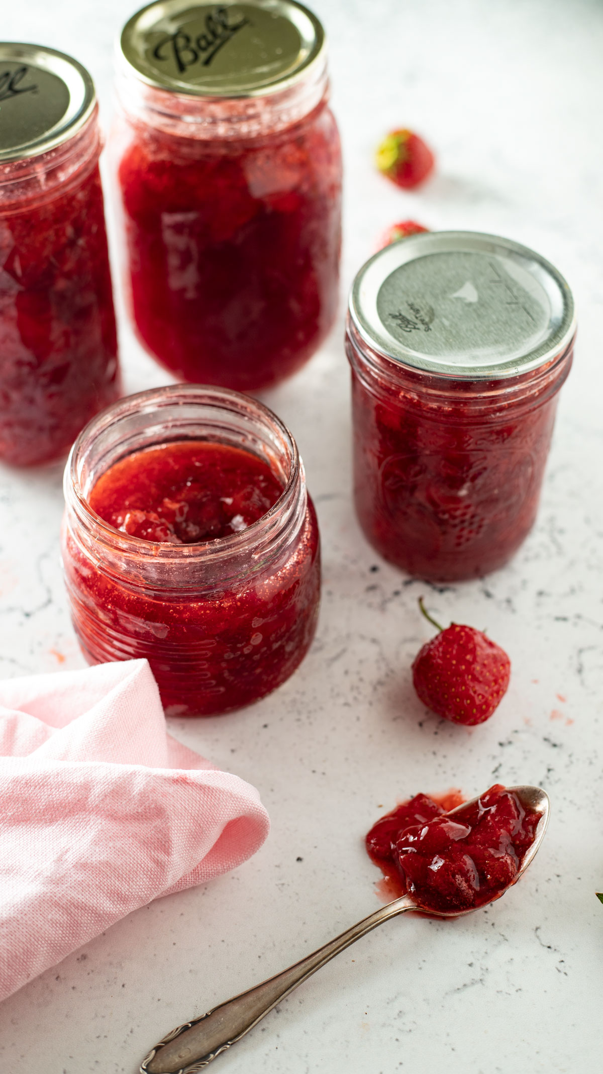 Spoonful of strawberry jam spilled over onto white board.