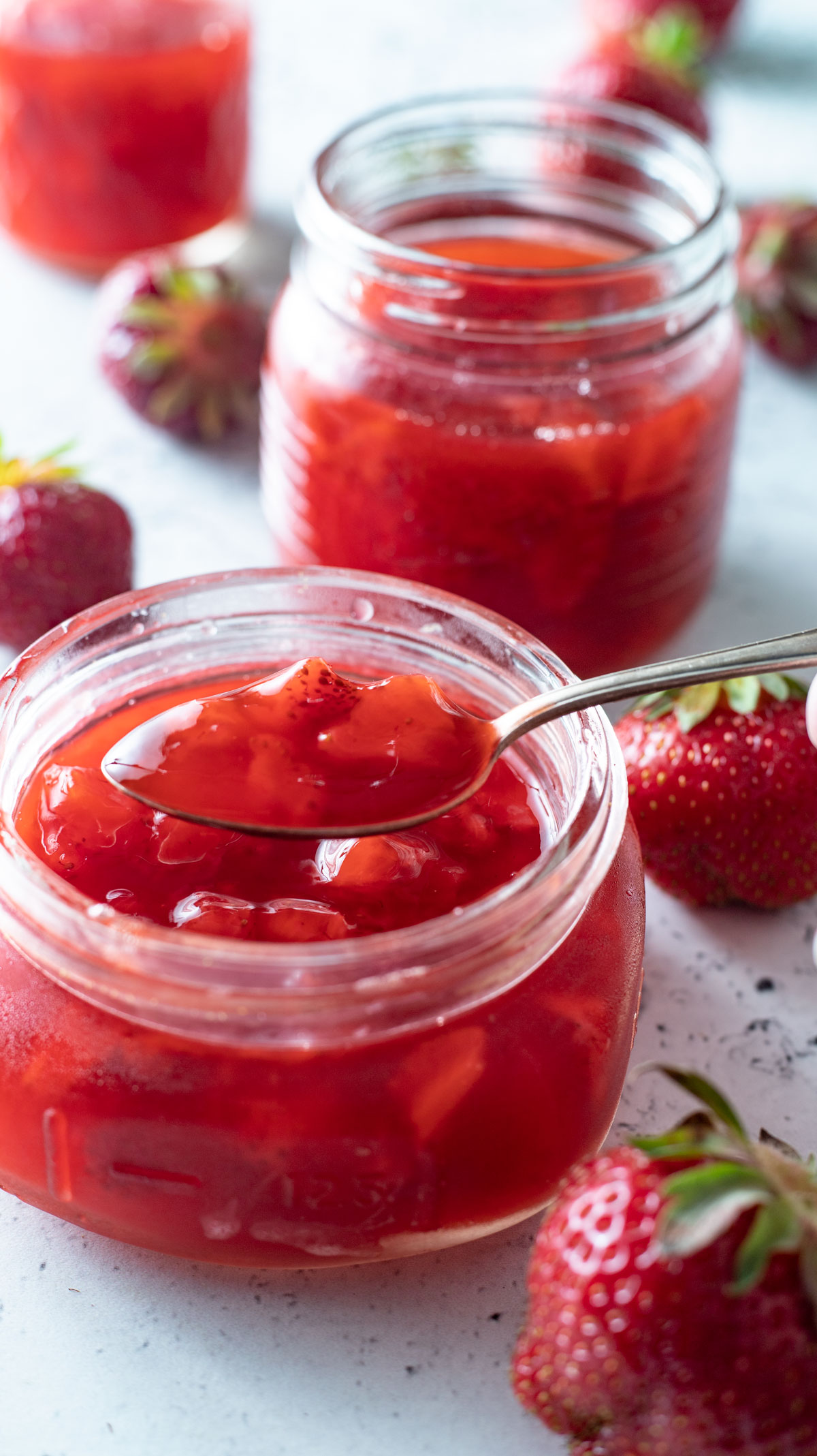 Jar of strawberry syrup with spoon resting in jar.