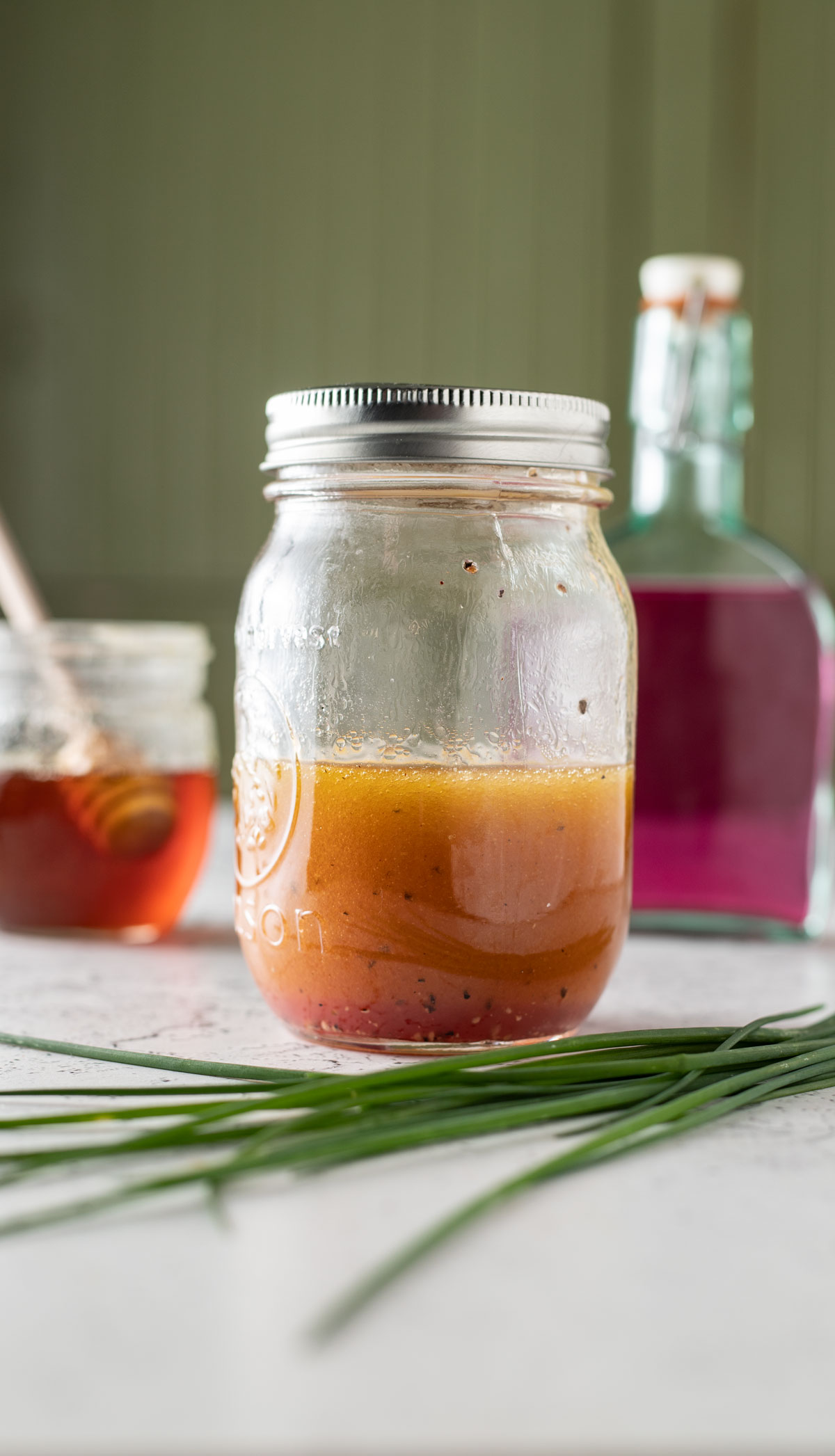 Chive dressing in a canning jar with honey pot and chive blossom vinegar.