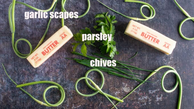 Garlic scapes, chives, parsley and butter on dark board.