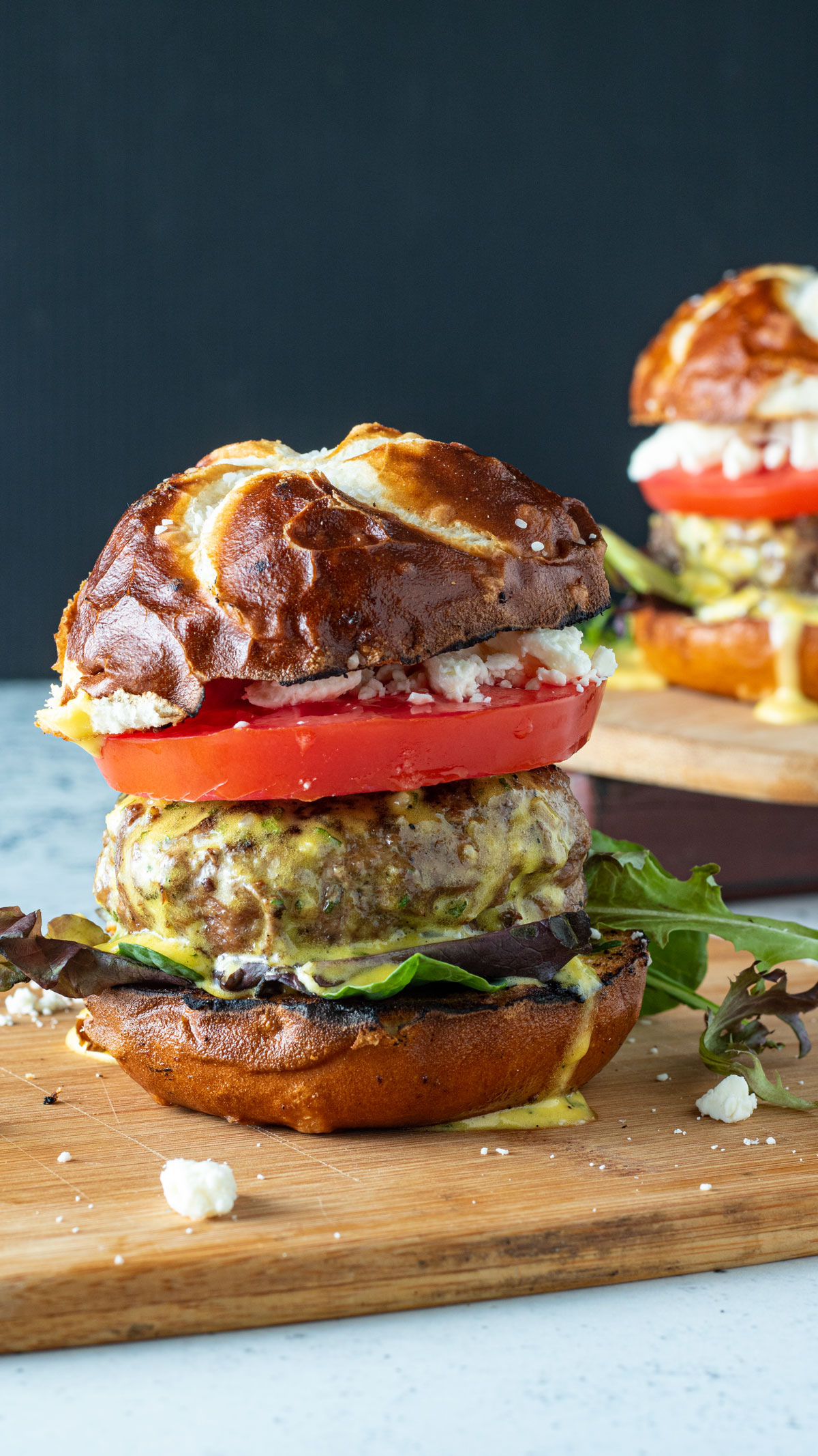 lamb burger with roasted peppers, cheese and top bun Juicy lamb burger on pretzel bun on wooden cutting board.