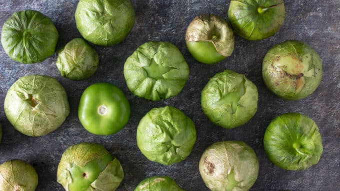 Overhead view of grouping of tomatillos on dark gray board.