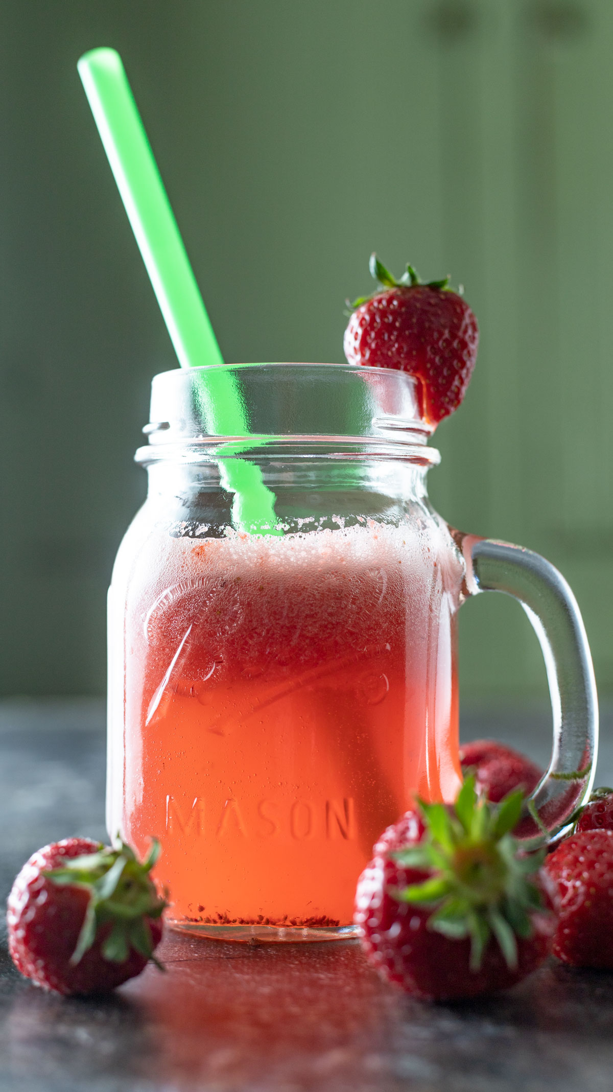 Ball jar with handle filling with sparkling strawberry juice garnished with strawberry and straw.