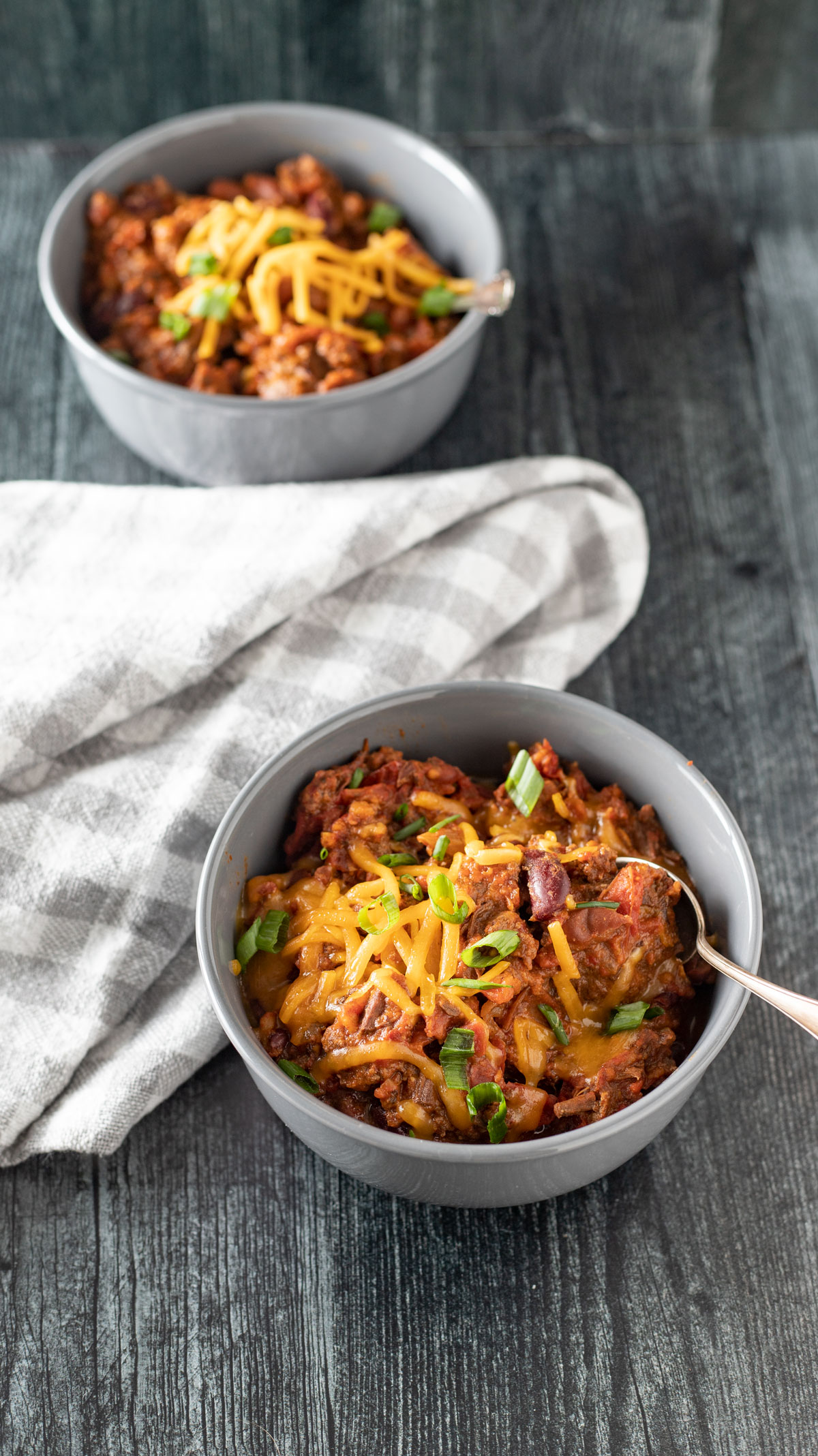 Two bowls of chili with toppings.