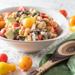 Colorful salad in a white bowl with multiple colors of cherry tomatoes, cucumbers, black olives and garbanzos.