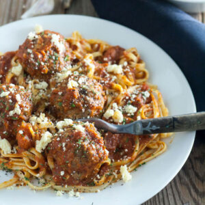 Venison meatball topped spaghetti in a white bowl.