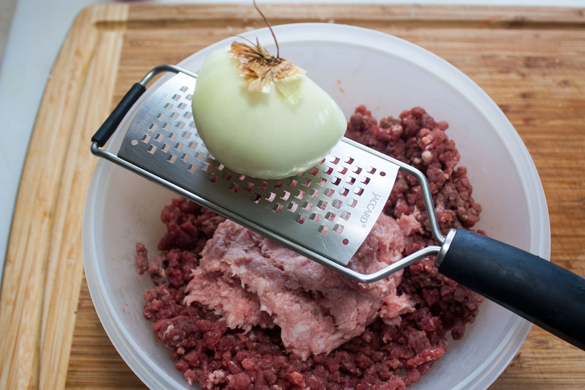Grating onion into the bowl with the meat.