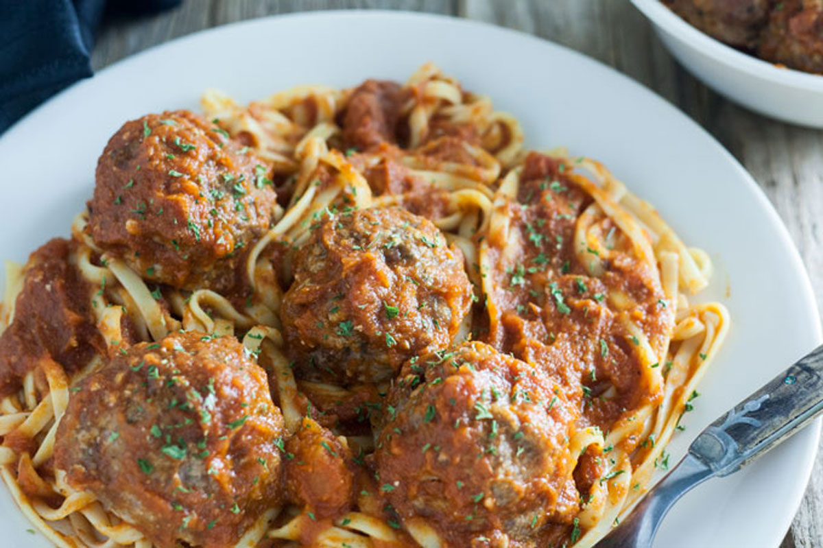 Close up of venison meatballs, smothered in sauce on a bed of pasta.