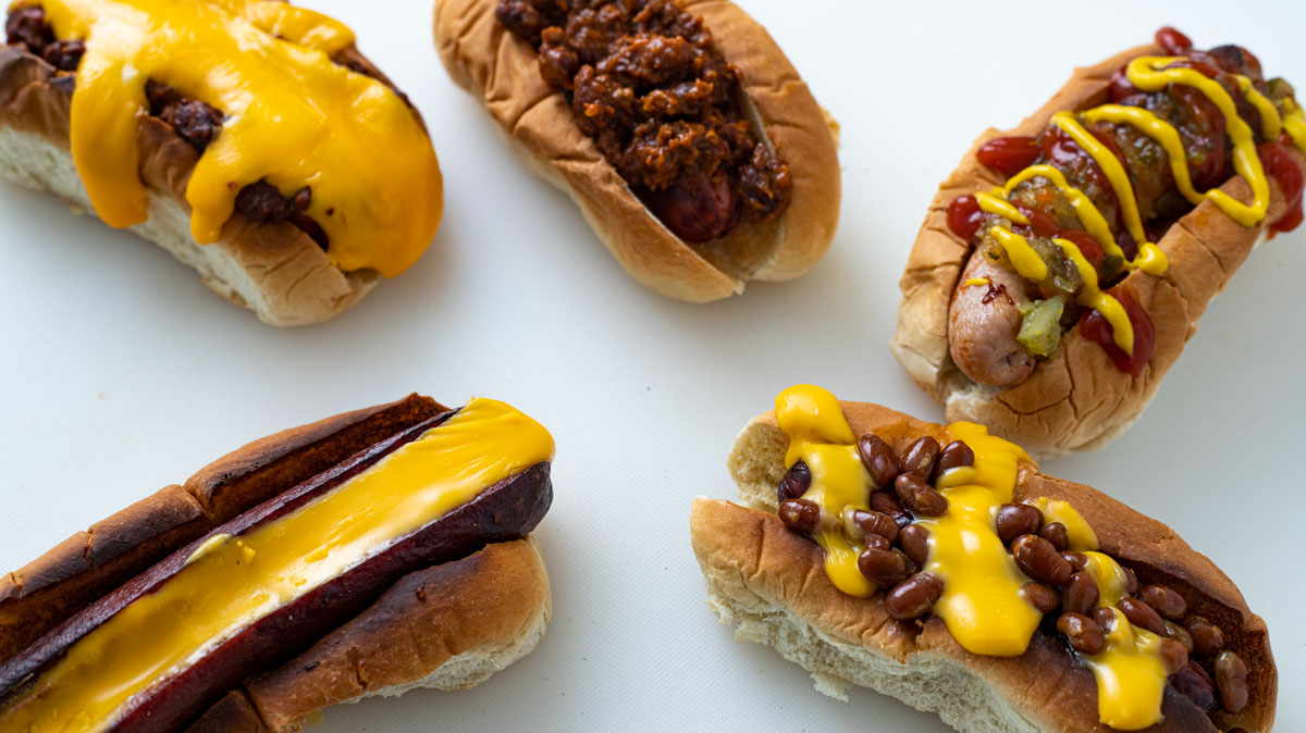 Five differently topped hot dogs on white board.