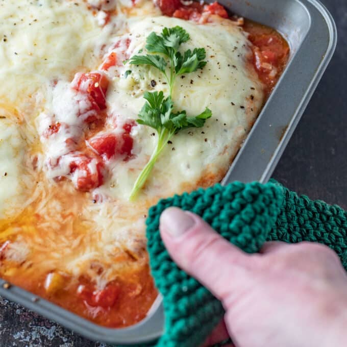Handing holding hot pad with casserole dish and colorful chicken
