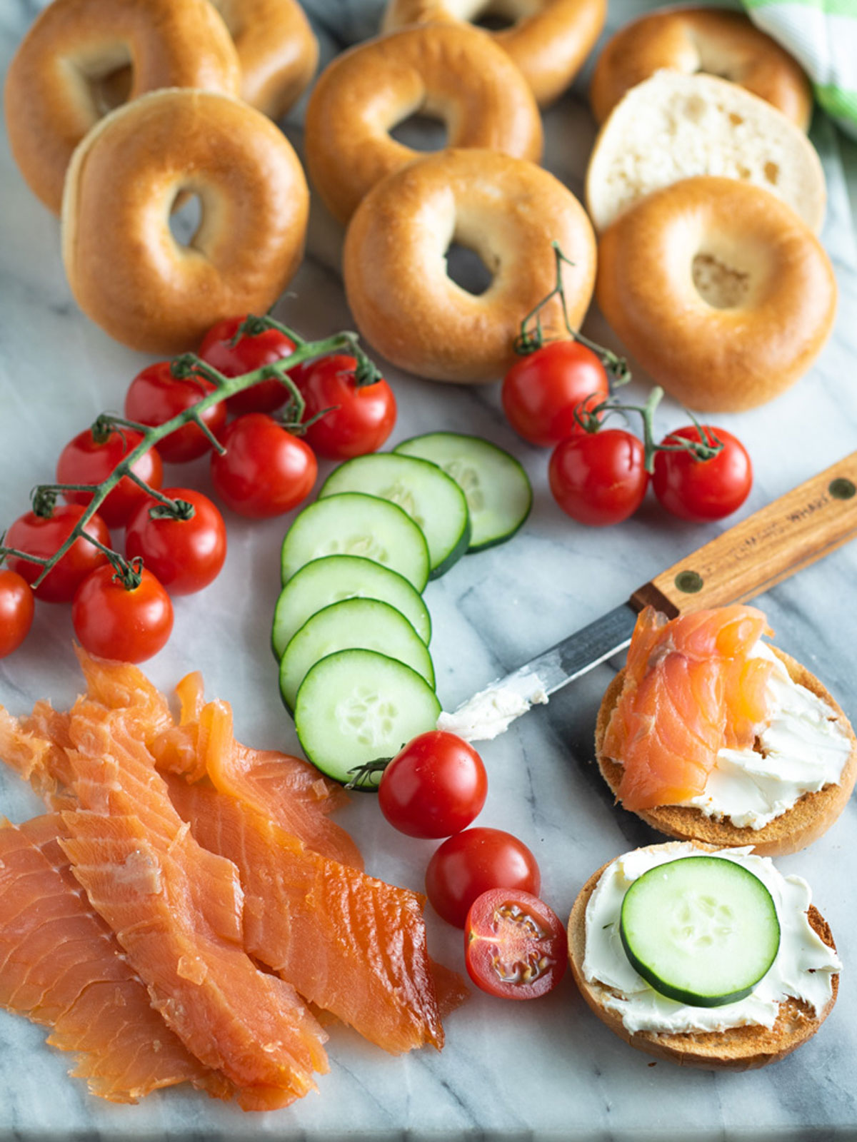 Sliced lox on board with colorful tomatoes and cucumbers.