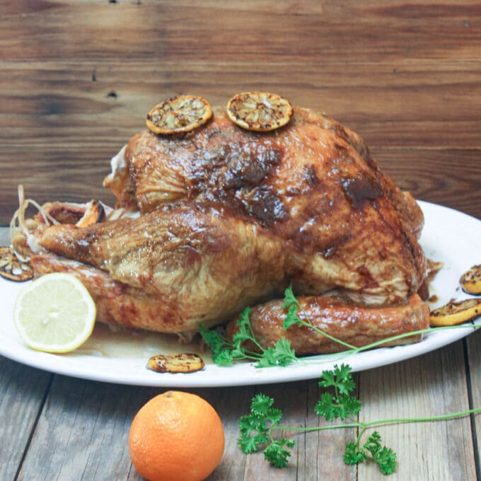 Whole roasted turkey on a platter with citrus fruits.