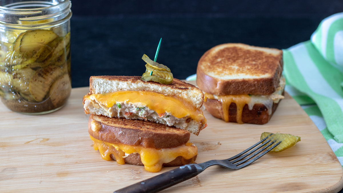 Tuna melt cut in half with a pickle sticking in the top with a toothpick.