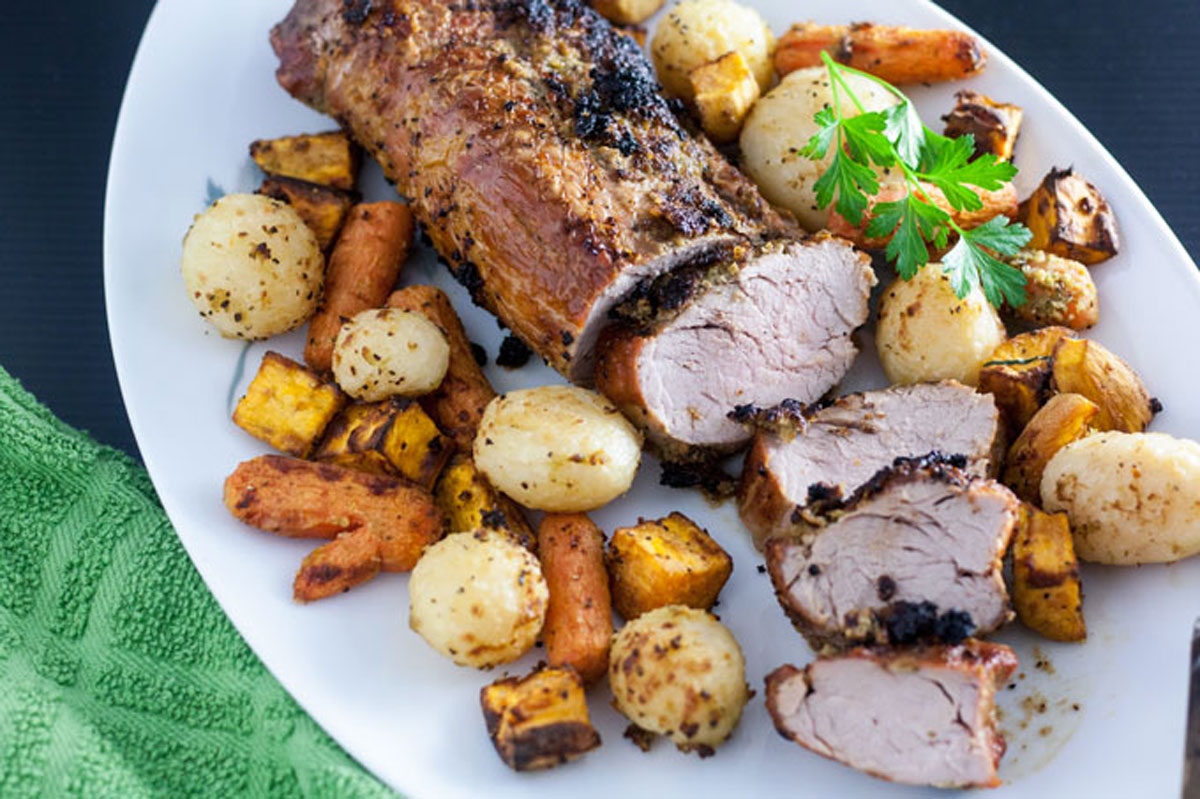 Sliced pork loin on a white platter with root vegetables.
