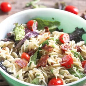 BLT pasta salad in green bowl with colorful tomatoes.
