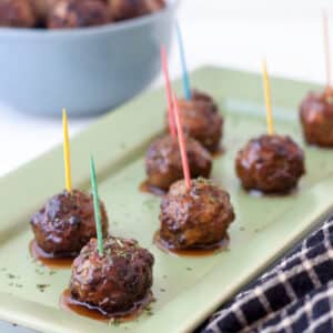 Cocktail meatballs on green tray with colorful toothpicks.