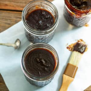 Open jars of cherry BBQ sauce with brush covered with sauce.