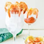 Shrimp arrange in cocktail sauce in a wine glass with ice.