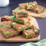 M&M cookie bars stacked on wooden board.