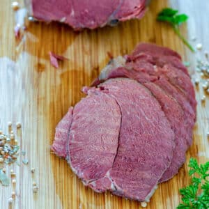 Slices of corned venison on bamboo cutting board.